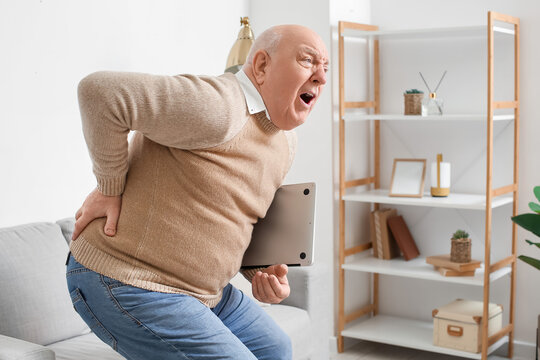Senior man with laptop suffering from back pain at home