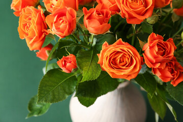 Vase with beautiful orange roses on green background
