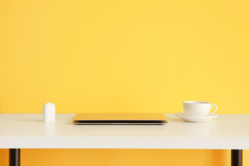 Workplace with modern laptop, earphones and cup of coffee near color wall