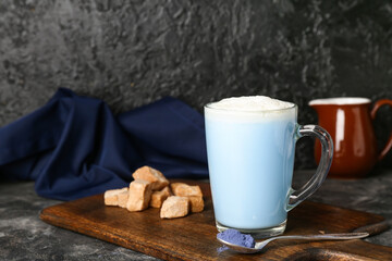 Wooden board with cup of blue matcha latte, powder and sugar on dark background