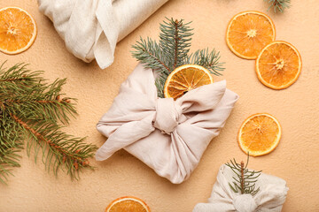 Composition with Christmas gifts wrapped in fabric, fir branches and dried orange slices on color background, closeup
