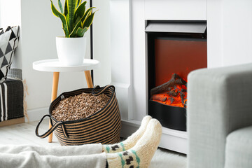 Bag with wood pellets and woman warming near fireplace in living room