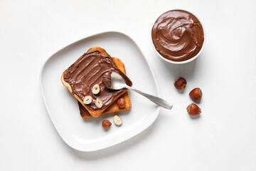 Plate of bread with chocolate paste and hazelnuts on white background