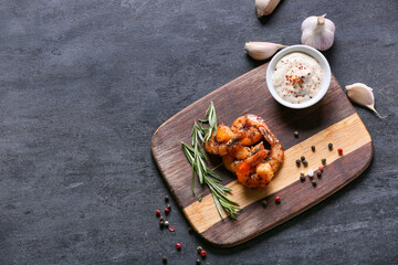 Wooden board of tasty shrimp tails and sauce on black background