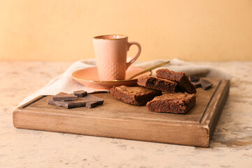 Wooden board with pieces of tasty chocolate brownie on beige background