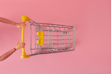 Puppet hands pushing a trolley from a supermarket on a pink background, minimalism concept
