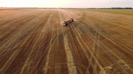 Obraz premium Tractor loader loads a haystack into a truck loaded with haystacks