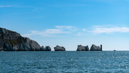 Naklejka premium View of Slow Cruise Boat Next to The Needles Lighthouse and chalk rocks in Alum Bay, Isle of Wight, United Kingdom