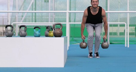 Fitness athlete man doing farmers walk with kettlebells training exercises outdoors at Athletics stadium outdoor gym. Strong male athlete strength training