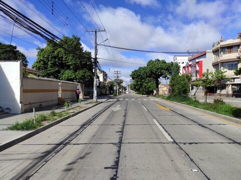 Avenida desierta vac&iacute;a con &aacute;rboles toborochi en camell&oacute;n, postes de luz, cables el&eacute;ctricos y un hombre en la acera bajo un cielo despejado con edificios en ambos lados de la calle