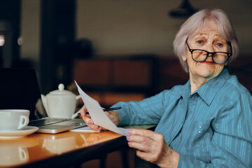 elderly woman with glasses sits at a table in front of a laptop Freelancer works unaltered