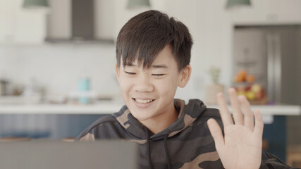 Asian preteen teen boy making video calling with laptop at home, using zoom online virtual class , social distancing, homeschooling, remotely learning during covid pandemic, new normal concept