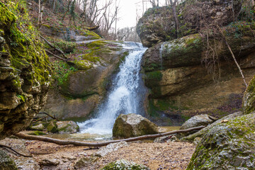 A mountain river in a natural channel with rapids and waterfalls in a natural park in late autumn.