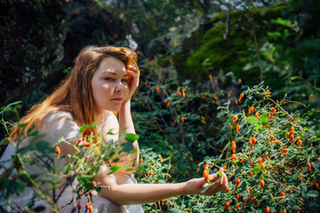 Beautiful dreamy woman in white dress  sitting among green rosehip bushes in summer forest....