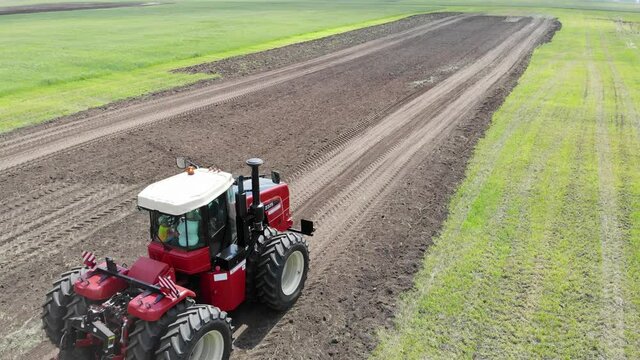 Red harvester drives across field and plows earth. Sows grain in field. He drives and leaves tracks in form of stripes. Russian field, harvesting, grain, agriculture, cultivation, modern technologies