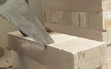 a man saws a block of foam concrete with a close-up of a hand and a hand saw..