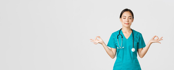 Covid-19, healthcare workers and preventing virus concept. Calm and patient asian female doctor, nurse in scrubs staying relaxed, meditating with eyes closed and happy smile, white background - obrazy, fototapety, plakaty