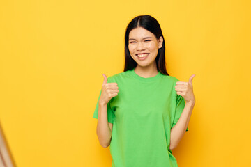 woman with Asian appearance in green t-shirts gestures with his hands emotions yellow background unaltered