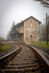 Fototapeta premium Villaverde de Pontones, Spain. December - 16 - 2021. A train track leads us to gaze at the Villaverde de Pontones Train Station on a foggy day