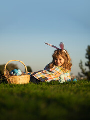 Child boy hunting easter eggs in spring lawn laying on grass. Cute bunny child boy with rabbit ears on sky background with copy space.