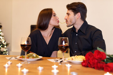 Smiling couple making spaghetti kiss together, celebrating