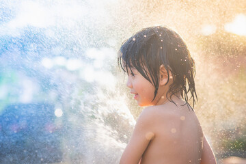 asian boy has fun playing in water from a hose outdoors