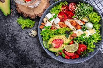 Healthy keto, ketogenic lunch menu with grilled chicken meat, avocado, feta cheese, quail eggs, strawberries, nuts and lettuce. Roasted chicken breast, fillet and fresh vegetable salad, top view