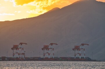 Sunset landscape view of container shipyard and cargo cranes at seaport in bay area with mountain...