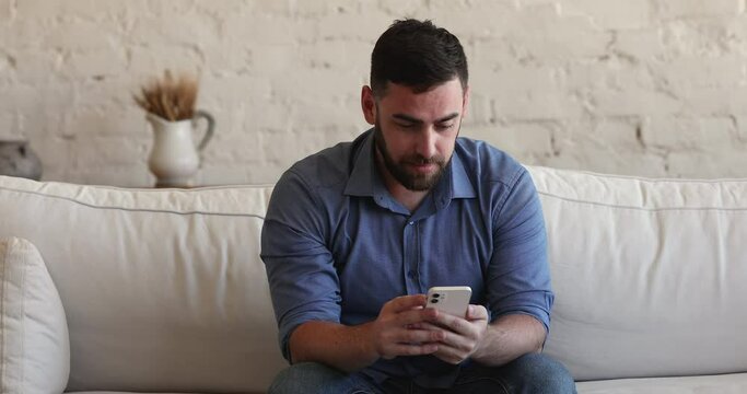 Online auction, betting lottery win, personal business achievement, hired at new job concept. Young 30s man sit on sofa at home read message, sms on cell phone feel overjoyed celebrate success concept