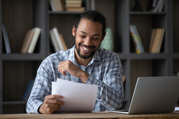 Happy cheerful African student guy reading admission letter from school, university, college, receiving paper document, smiling, laughing. Millennial businessman getting good deal, contract