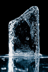 Crystal clear natural ice block in cold blue tones on a black reflective surface. - 480681908