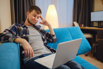 Bored young guy sitting near laptop, daydreaming, thinking about something during online work at home office. Millennial Caucasian man having dull remote job