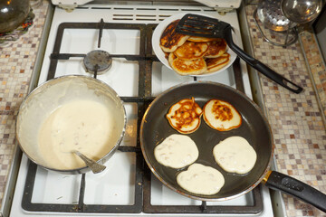  Pancakes are fried in a large frying pan on a gas stove.