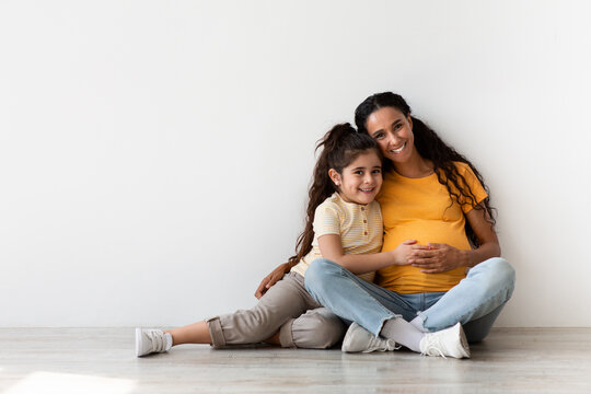 Happy Expectation. Smiling Pregnant Woman And Her Little Daughter Cuddling Together