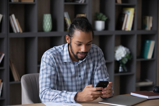 Focused Busy Millennial Black Business Man Browsing Internet On Smartphone, Using Online App, Reading Text Message, Sitting, Working At Home Office Workplace Table, Making Telephone Call