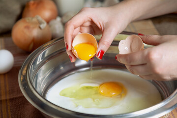 Female hand pouring yolk of egg from half of shell..