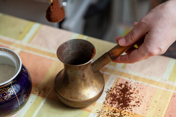 Fototapeta na wymiar Hand pouring ground coffee into cezve close-up..