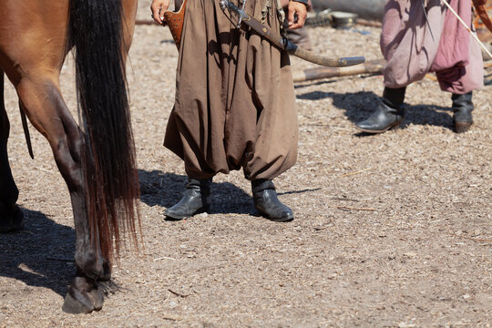 Vintage warrior in wide pants stands next to horse