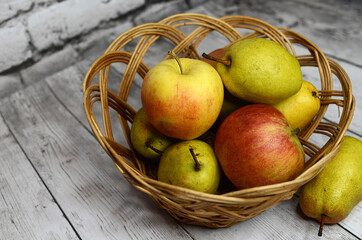 Ripe apples and pears in a wicker basket against the background of a white brick wall.