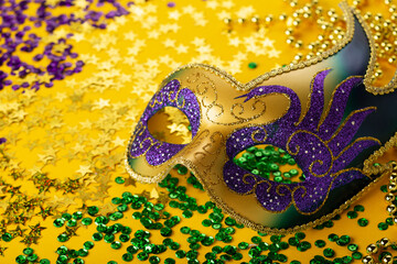 Mardi Gras Luxury Masquerade venitian festival carnival mask, gold color beads and golden, green, purple confetti on yellow background.