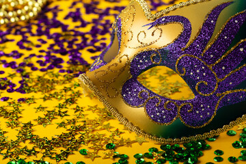 Mardi Gras Luxury Masquerade venitian festival carnival mask, gold color beads and golden, green, purple confetti on yellow background.
