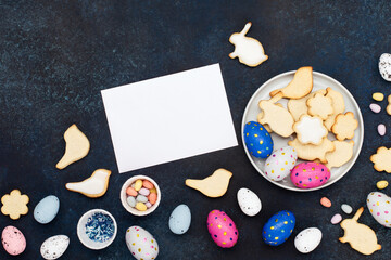 Fototapeta na wymiar Festive homemade Easter cookies, chocolate eggs, sugar sprinkling on dark blue wooden background. Happy Easter concept. Copy space, top view.