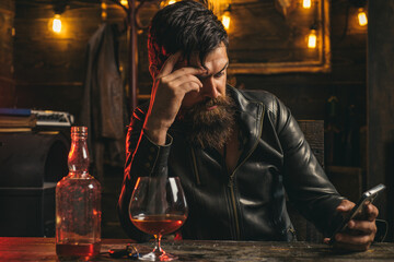 Handsome bearded businessman is drinking expensive whisky. Social media addiction, alcohol abuse.