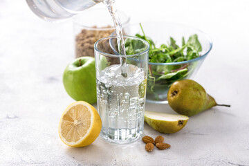 Clean fresh water is poured into a glass beaker while standing on table with fruits, granola and salad bowl on wooden table. Healthy breakfast. Food set for diet and healthy food