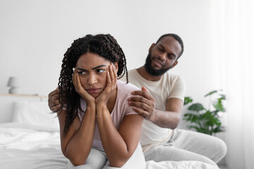 Millennial african american husband calm his wife, sit on comfort bed in bedroom interior
