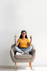Look At This. Happy Brunette Lady Sitting In Armchair And Pointing Up