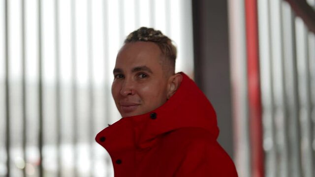 Close-up portrait of a handsome gay man walking in winter in a red jacket through the streets of the city. Looks at the camera and smiles.