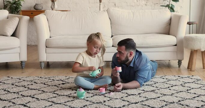 Preschool cute blond girl play with dad at home, use plastic toy dishware, prepare tea, pour imaginary sugar. Father spend carefree weekend leisure with adorable caring daughter. Playtime, fun concept
