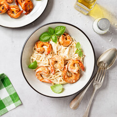 Pasta spaghetti with grilled shrimp and creamy alfredo sauce served with fresh basil leaves. Light gray background, top view
