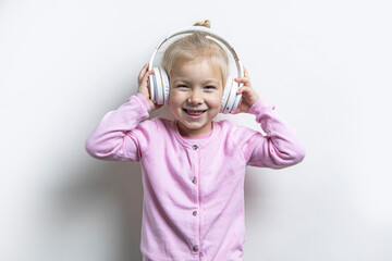 Smiling child girl in white headphones on a light background.